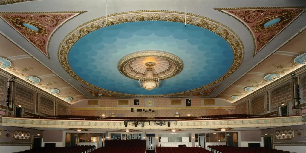 a circular blue light around a candleabra in the center of a theatre ceiling