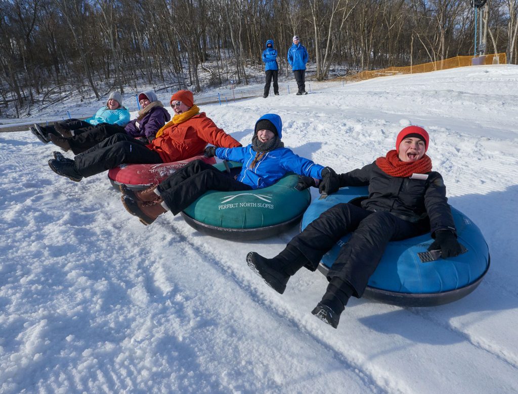 a line of five young people snow tubing down a hill together