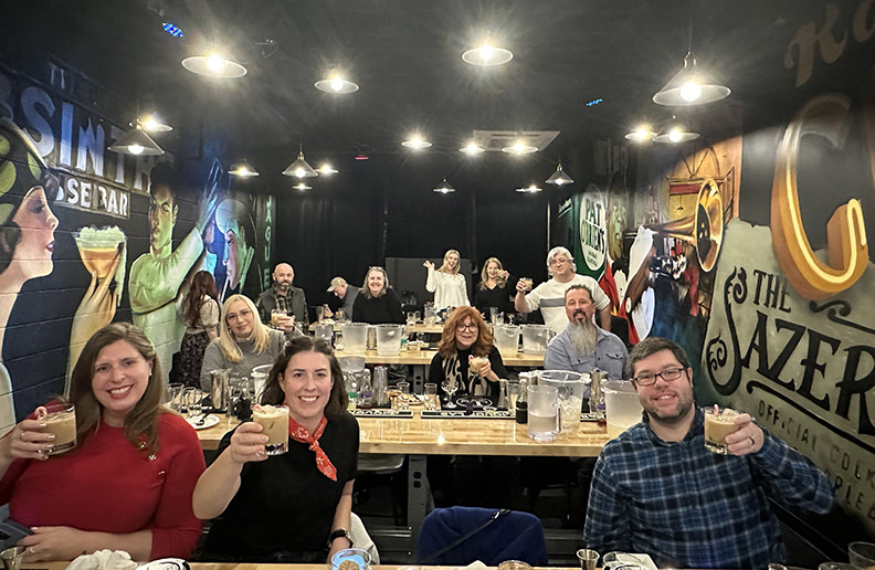 A large group of people at a bar holding drinks in hand