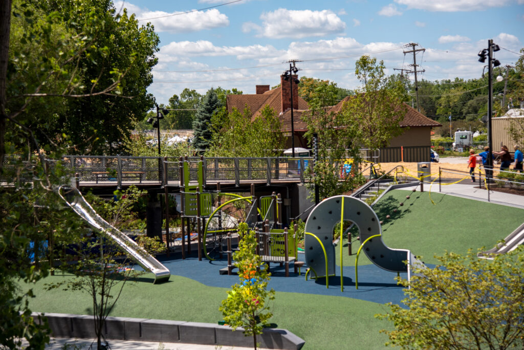 a city park with a walkway bridge overhanging the shallow play area underneath