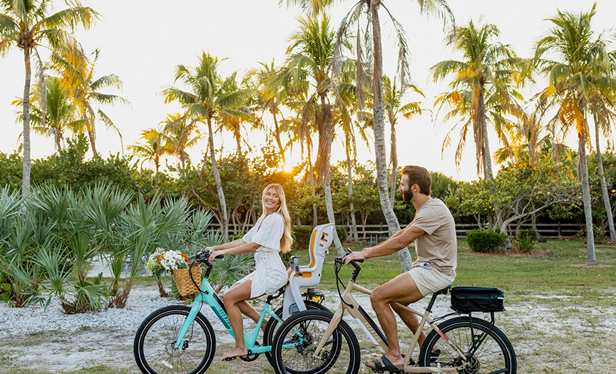 man and woman riding bikes together with palm trees in background