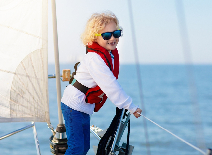 a blond child on a parasail. she's wearing sunglasses and obviously she's wearing a life jacket