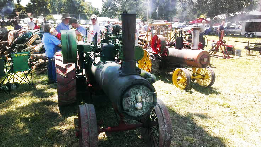 an antique steam engine sitting on a fairground with other old tractors