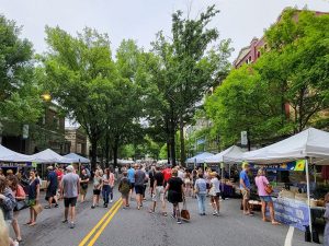 Greenville Farmer's Market. There are people walking down the center of a street with market vendors lining both sides.