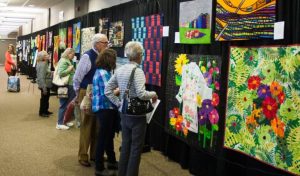 Three people looking at some quilts that are on display at a quilt show