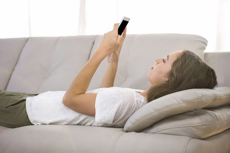 woman in white shirt laying on sofa playing with cell phone