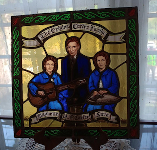 stained glass window, two women holding guitars and one man standing in the middle