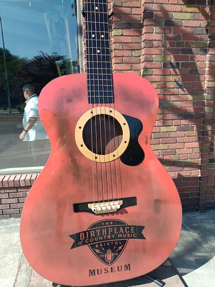 a giant acoustic guitar sitting on the sidewalk in front of a music museum 