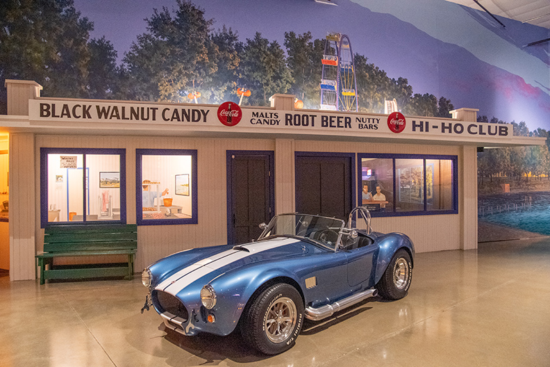 blue classic convertable race car parked in front of a root beer stand