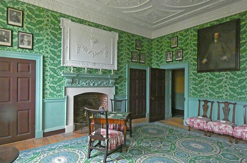 Light green room with chair, an empty fireplace and decorated molded plaster ceiling 