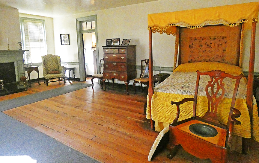 antique poster bed with yellow cover and bedspread in large wood-floor bedroom