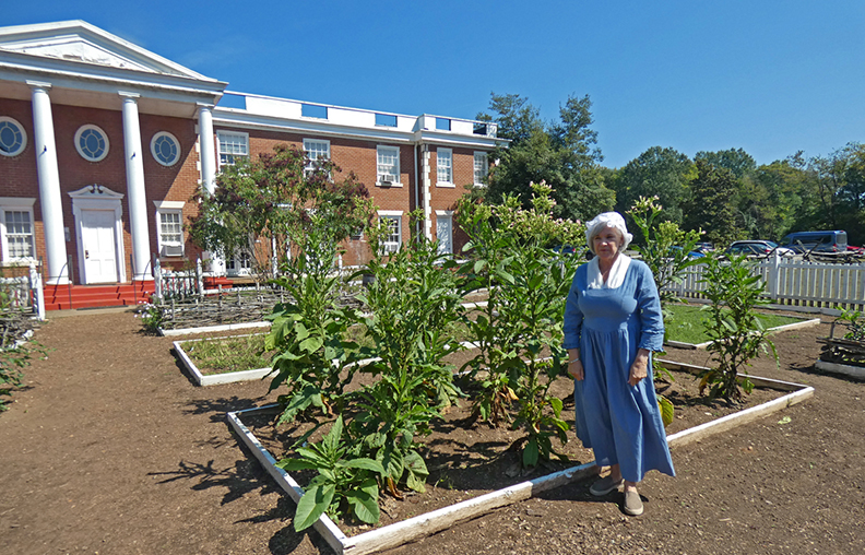 lady in glue dress stands in front of a garden