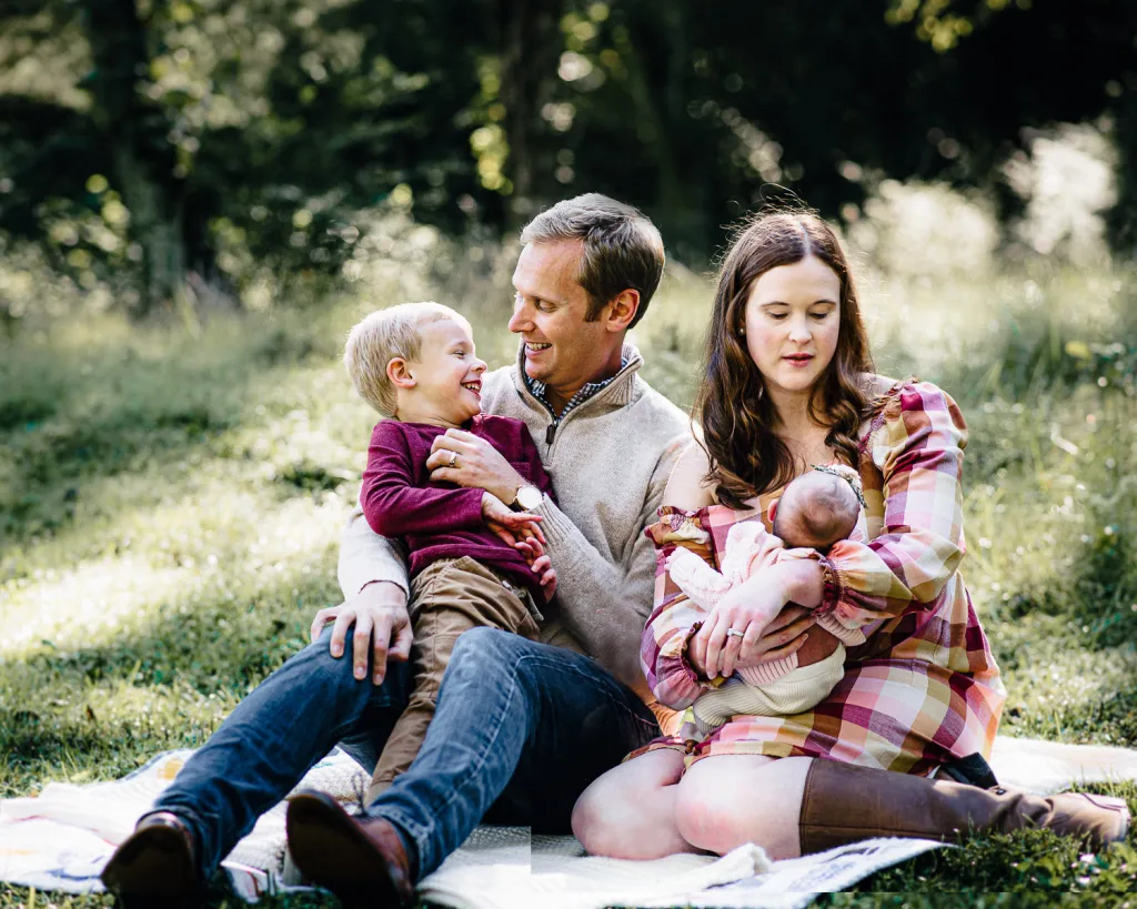 a couple sitting outside on a blankt with their babies