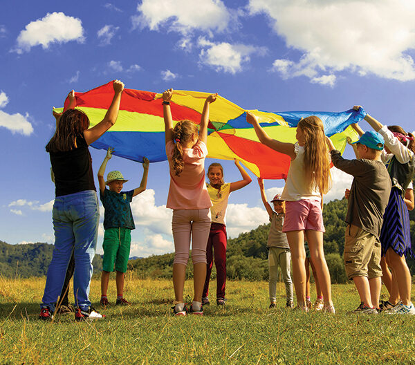 a circle of kids holding huge multi-colored flag above their heads