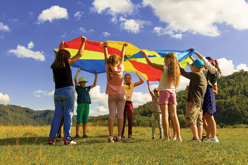 a circle of kids holding huge multi-colored flag above their heads