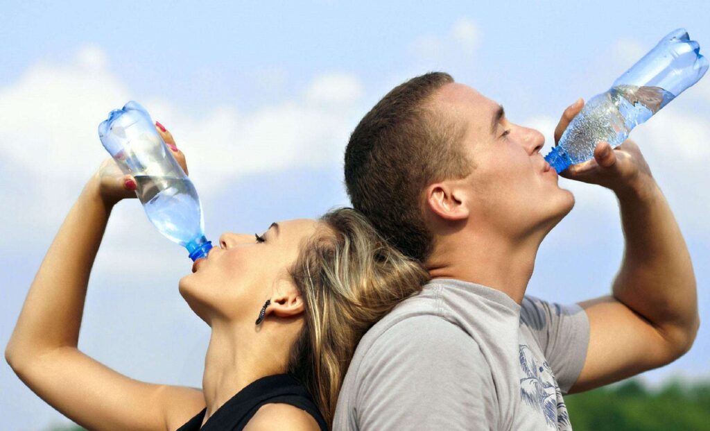 man and woman standing back to back & drinking a bottle of water