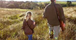 Child walking through a field with their parent on a hunting trip