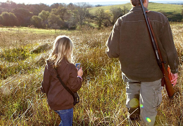 Child walking through a field with their parent on a hunting trip