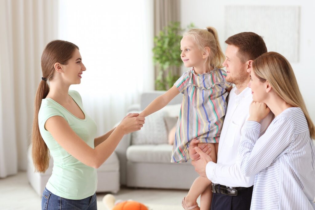 Man holding daughter with wife and introducing her to babysitter.
