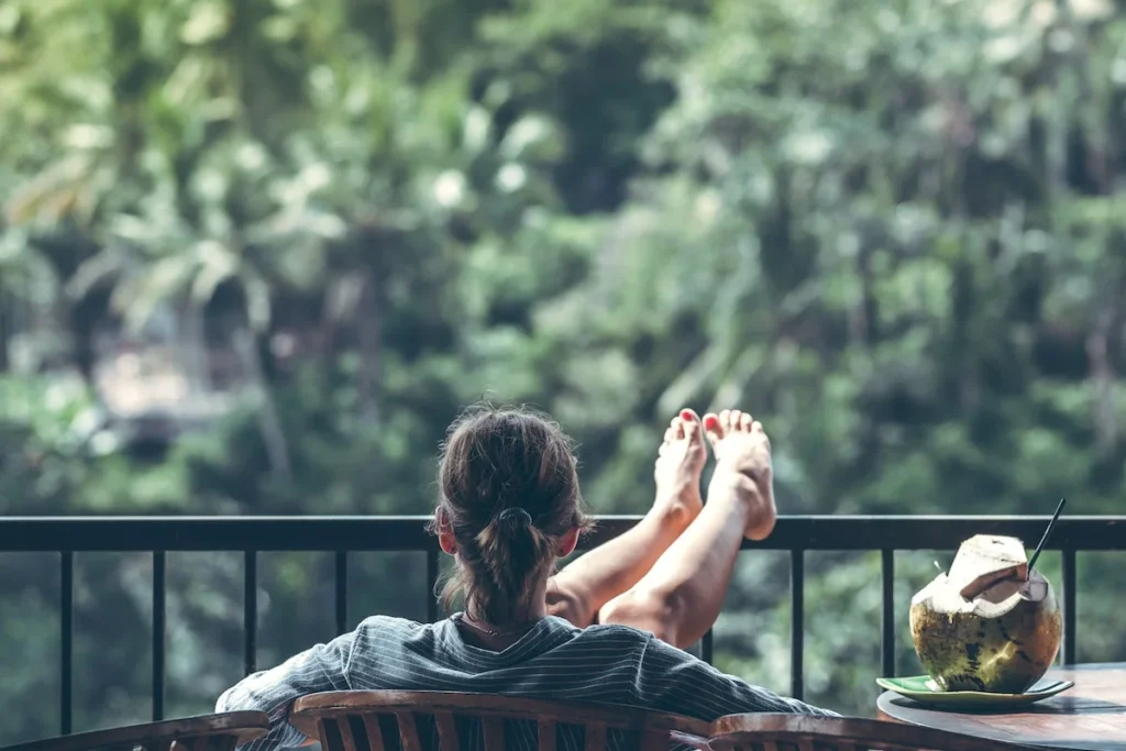 A lady with feet up on the portch railing relaxing overlooking trees and quiet