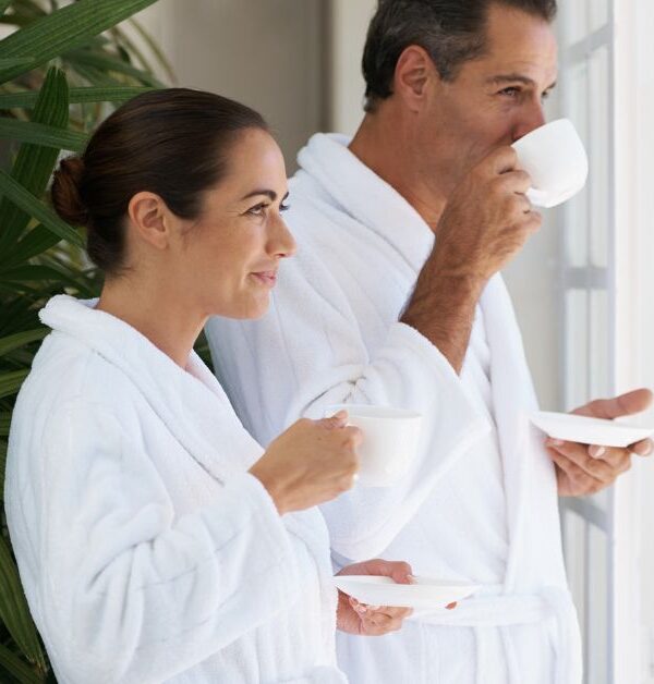 A couple in white robes looking out a window drinking coffee