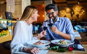 a couple siting at a table in restaurant and holding wine glasses