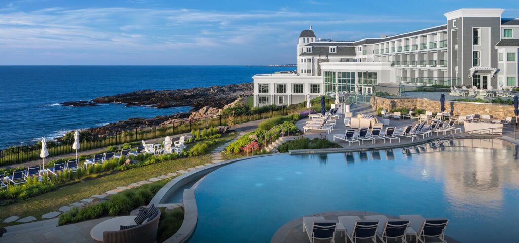 infinity pool in front of white buildings of Cliff Huse in Maine, ocean view at left. 