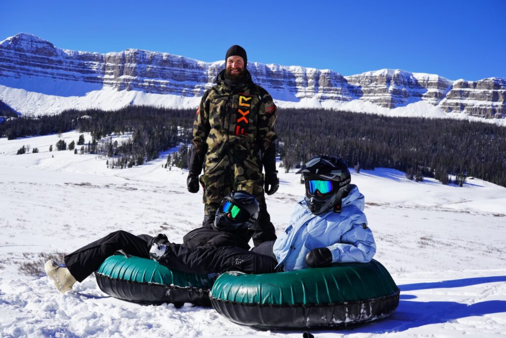 2 kids snow tubing with an adult standing by