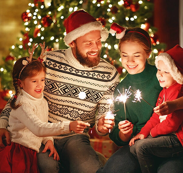 family in front of christmas tree holding lit candles