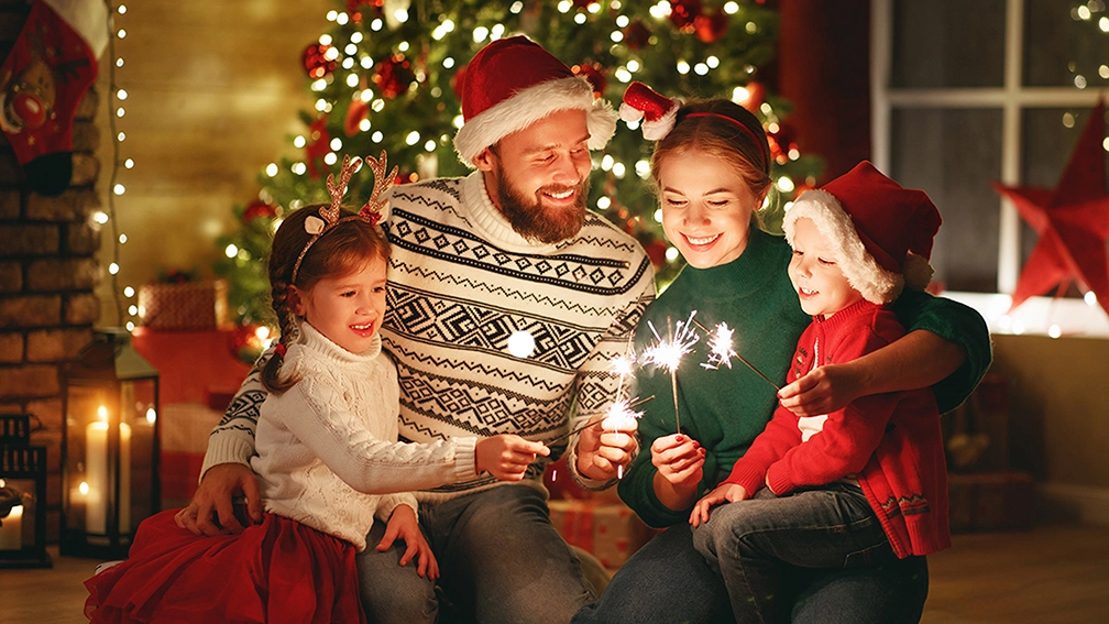 family in front of christmas tree holding lit candles