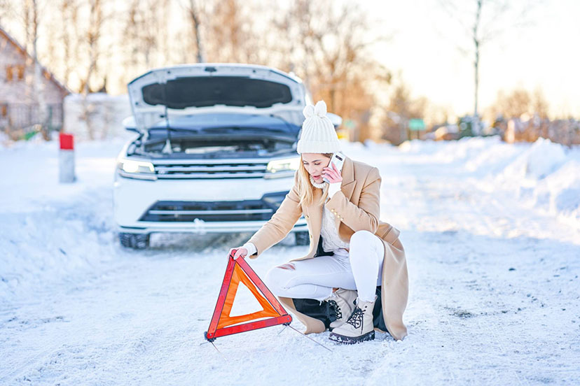 a car at side of road in snow with driver setting out a warning triangle sign