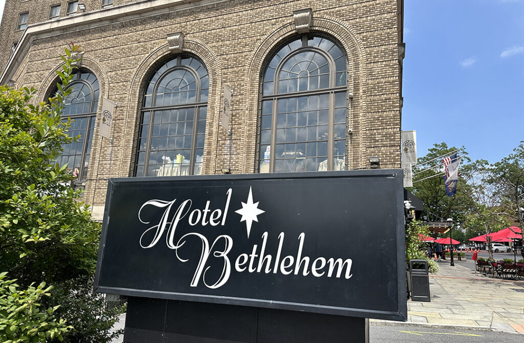 two-story brick building with three stain glass windows with rounded tops. Hotel Bethlehem sign in black in front of it. 