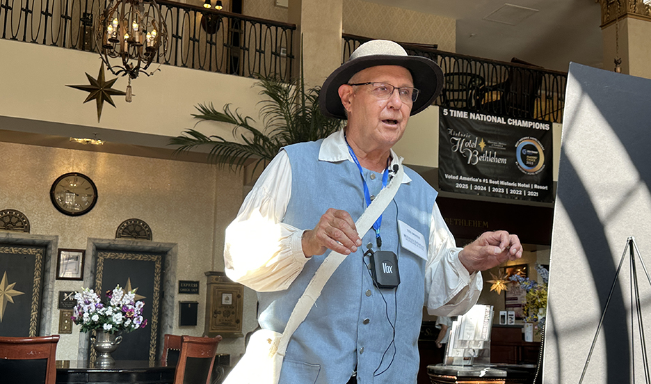man with glasses in a blue vest and white tour hat standing inside a historic hotel