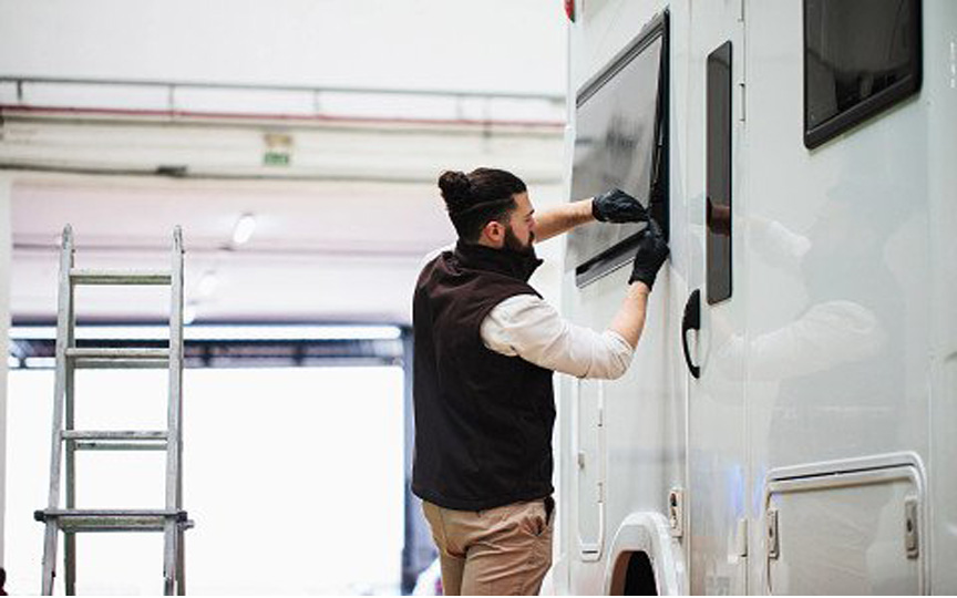 Man in vest and sweater hat checking a rectangle window to his RV