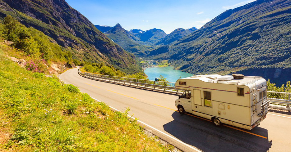 white RV headed toward the left with mountains and river in the background