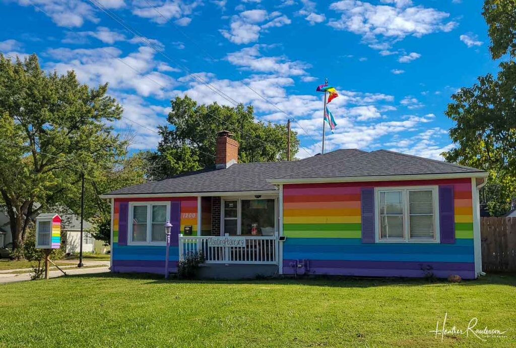 a single story residential house painted with the rainbow colors in horizontal stripes 
