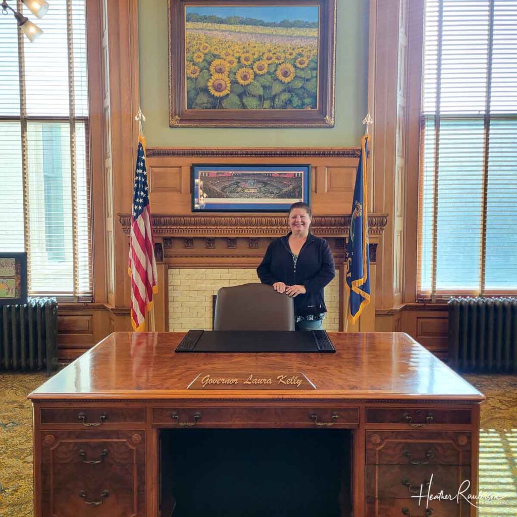 a brown flat empty wooden desk of a governor with a lady standing behind it and in front of a fireplace like in an office
