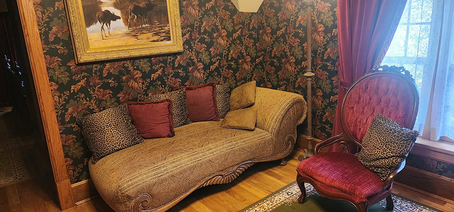 an antique leather covered settee with burgandy square pillows against a flower printed wall in a b&B