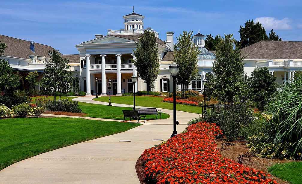 A white colonial two-story building with pillars on the front and a winding walkway to the front of it.. 