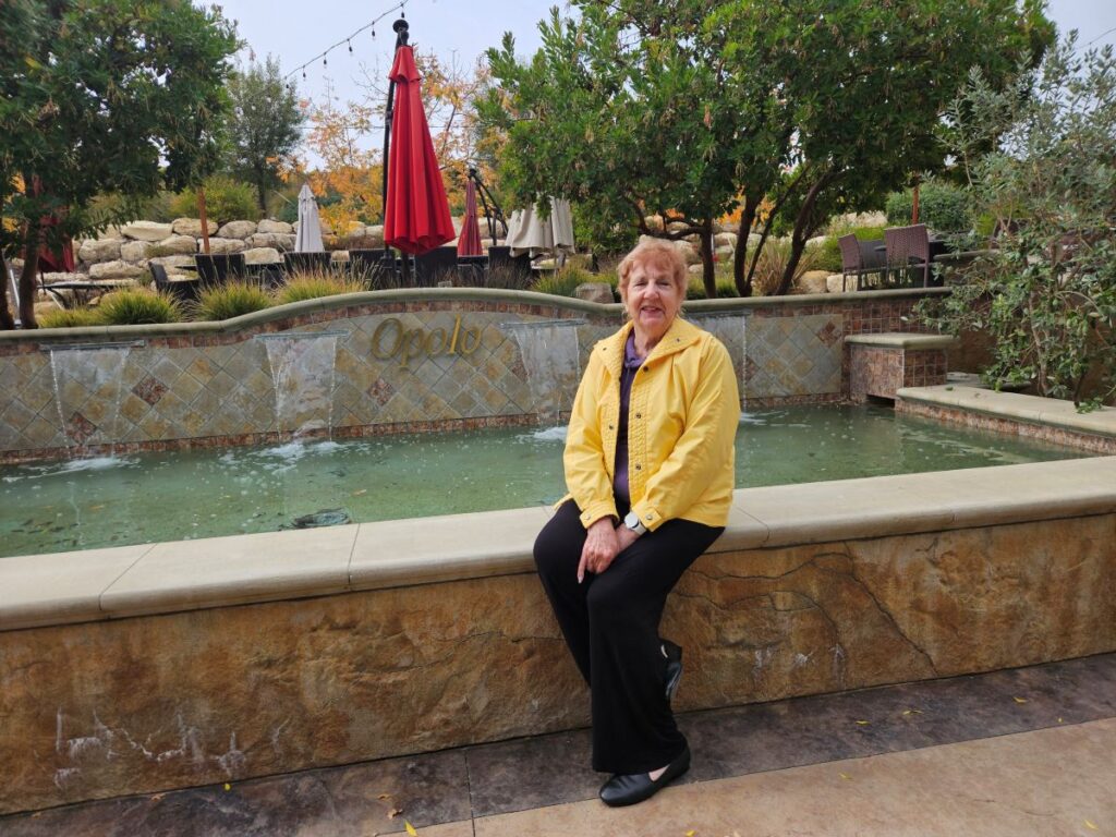 lady with yellow jacket sitting on a flat rock wall edge of a pool of water