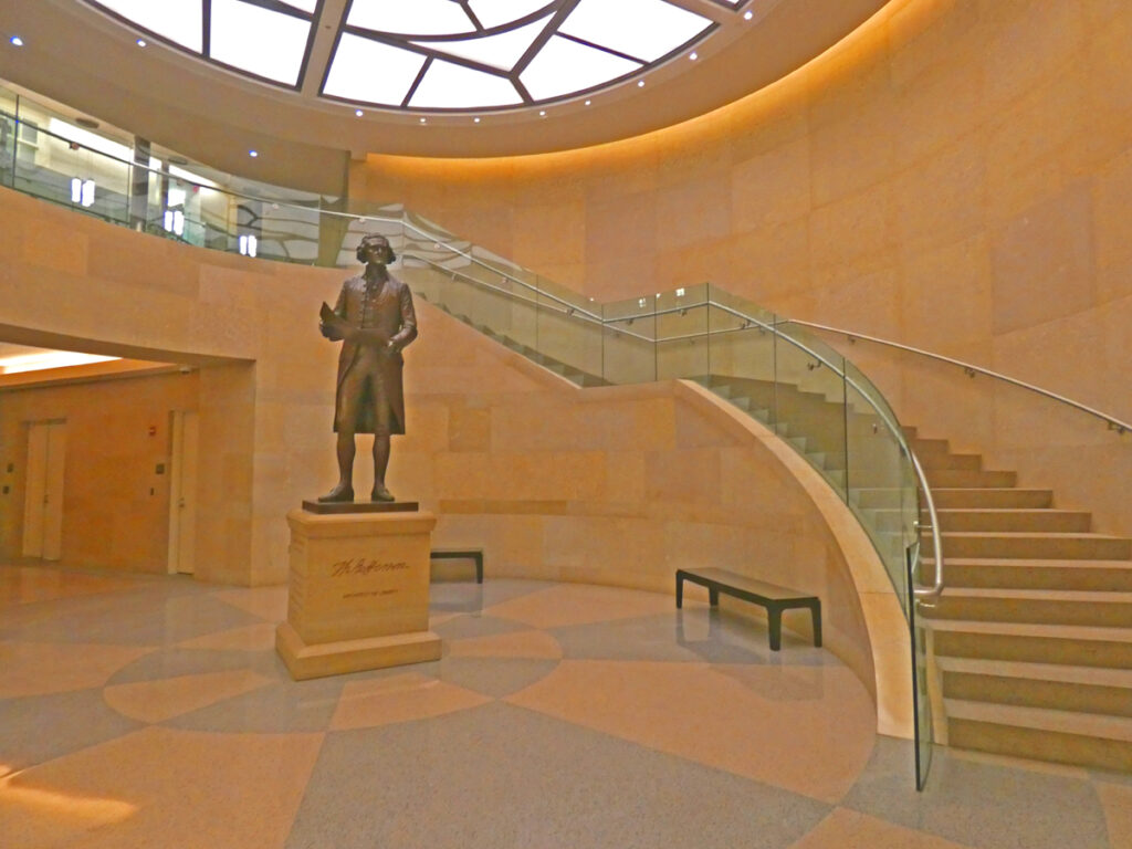 A statue of Thomas Jefferson stands in front of a curved stairway 