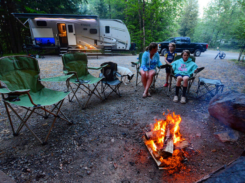 Family sitting around a campfire with an RV behind them