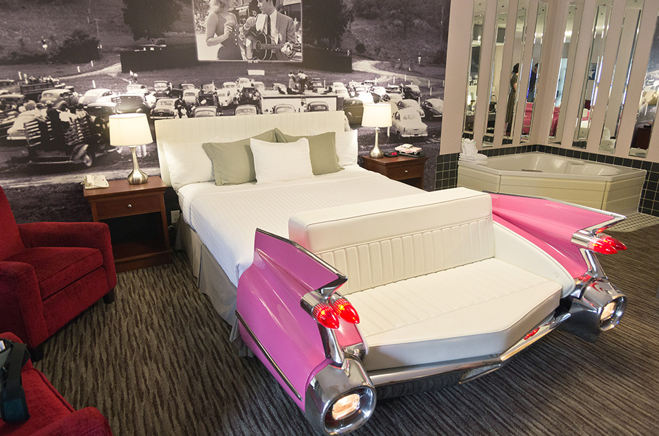 A double bed designed like a pink cadillac facing toward the wal painted like a drive-in theatre 