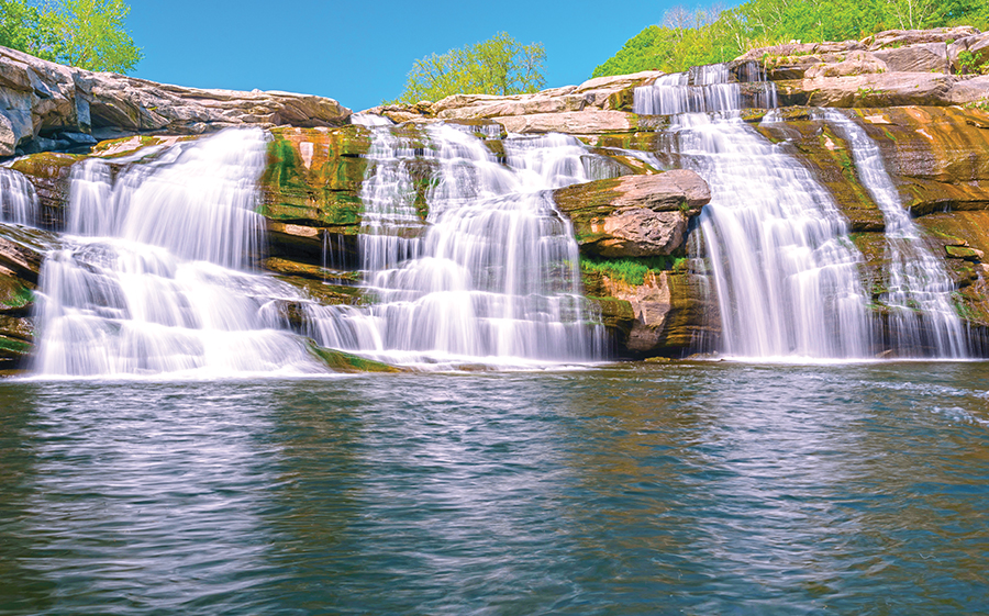three waterfalls over a small cliff into water in the front