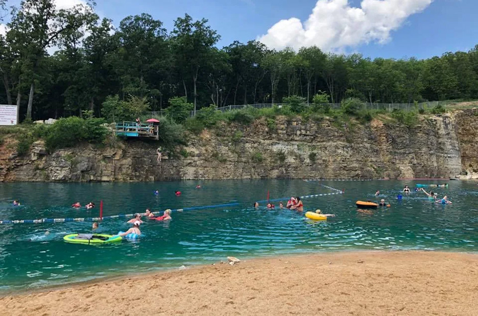 a beach in front of a small lake created in a former rock quarry for swimming 