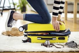 Someone kneeling on a suitcase to help it close
