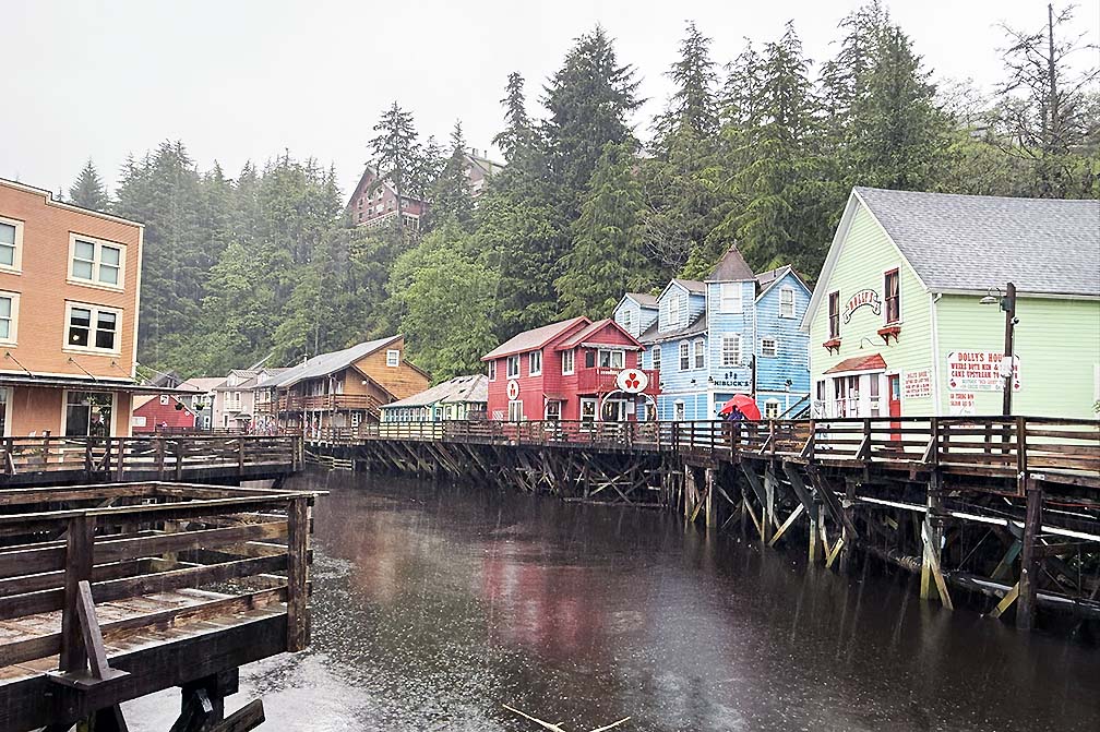 multi pastel colored cottages lined along a river with railings on both sides and trees and hils in background