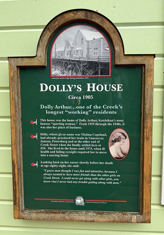 A dark green rectangular sign on the side of building wall that says Dollys