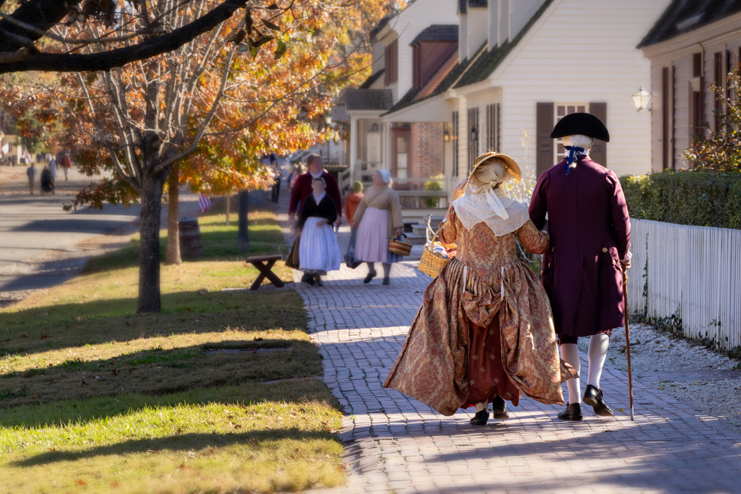 People dressed in colonial attire walking on sidewalk. 