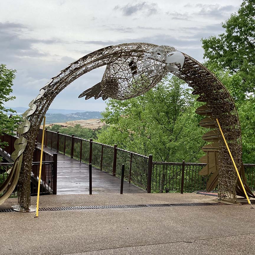 An arch gateway at the entrance of a nature trail with a wire sculpture of an eagle at top 